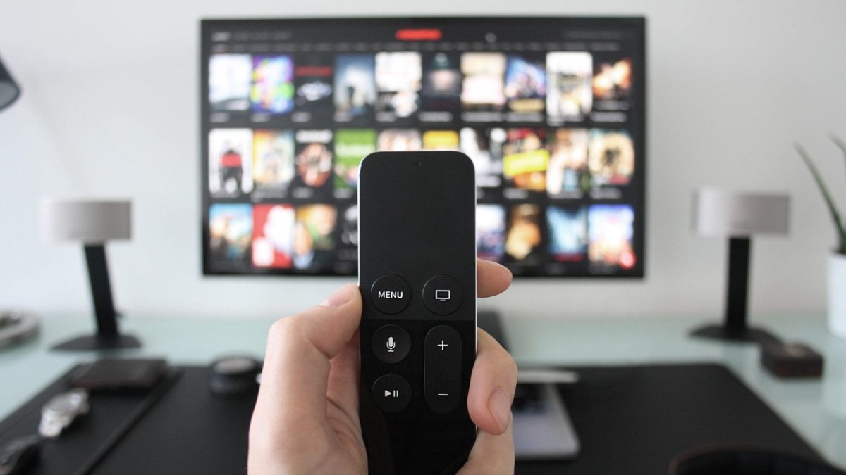 日剧tv 深色客厅环境里电视屏幕正在播放日剧画面，屏幕右下角显示缓冲进度环，茶几上放着遥控器与打开的笔记本